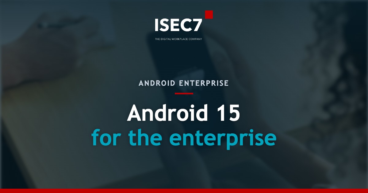 A person holds a smartphone displaying the Android 15 logo on the screen. In the background, a second person is seen writing on a notepad with a pen. The scene takes place at a table in an office setting.